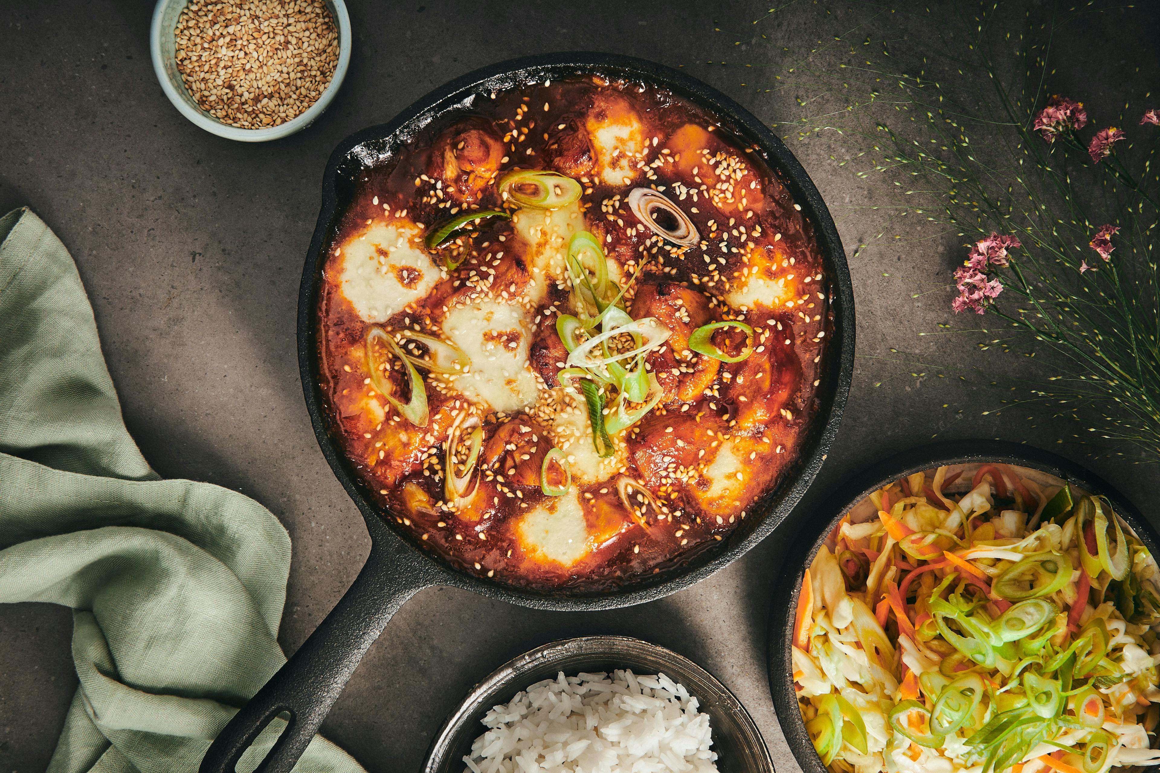 På billedet ses et herligt eksempel på en traditionel koreansk ret: buldak – ildkylling med gochujang, mozzarella, sesamfrø og koreansk coleslaw. I retten bruges gochujang som en base for en velsmagende ingefærsauce, der giver kyllingen sin stærke og rige smag.